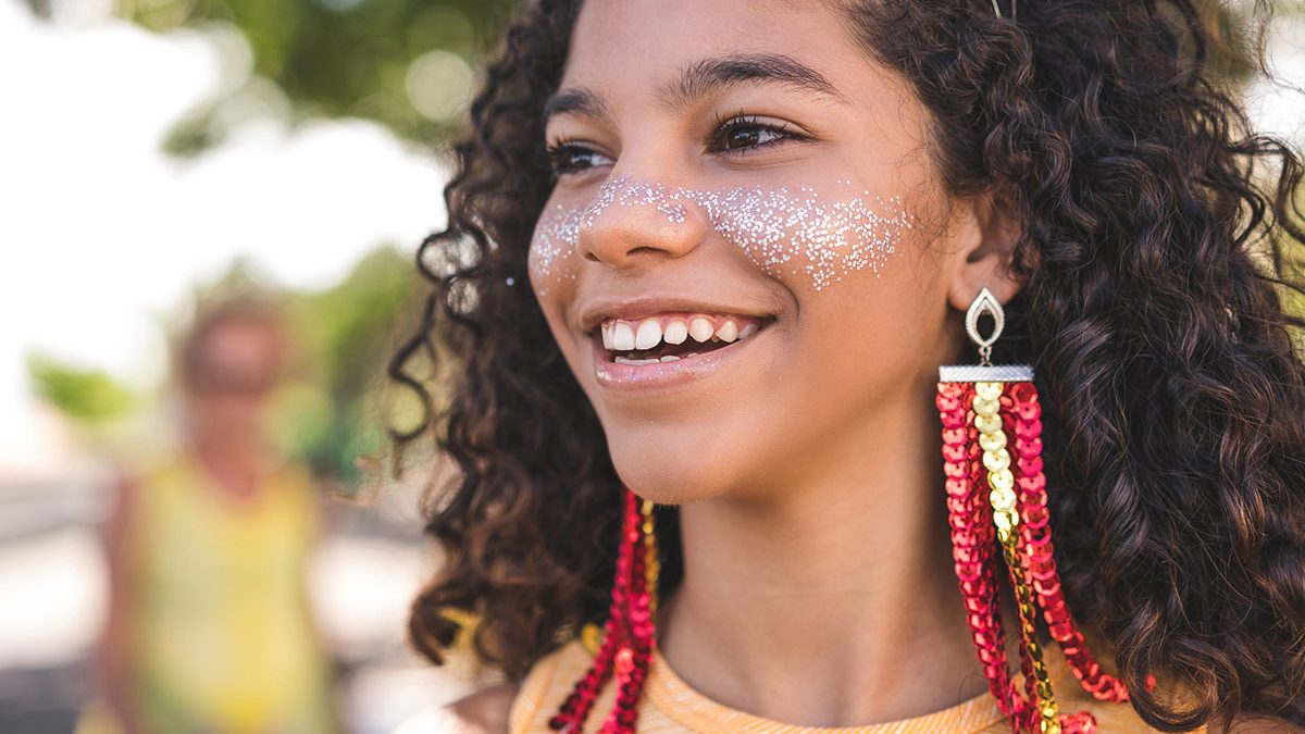 Criança com cabelo encaracolado e glitter e maquiagem no rosto durante Carnaval