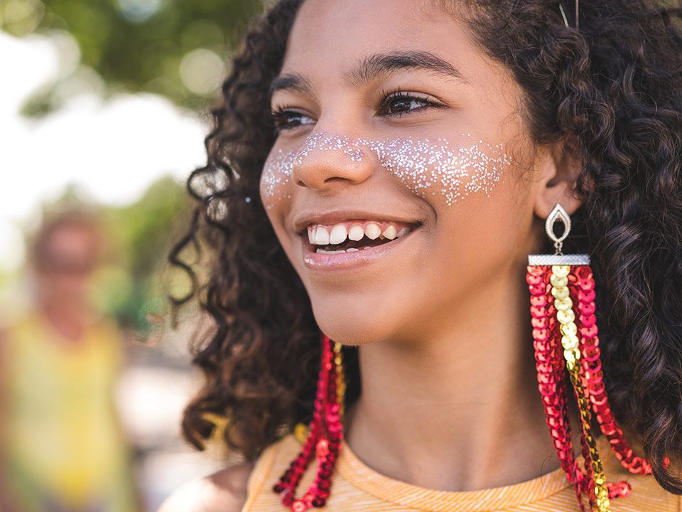 Criança com cabelo encaracolado e glitter e maquiagem no rosto durante Carnaval