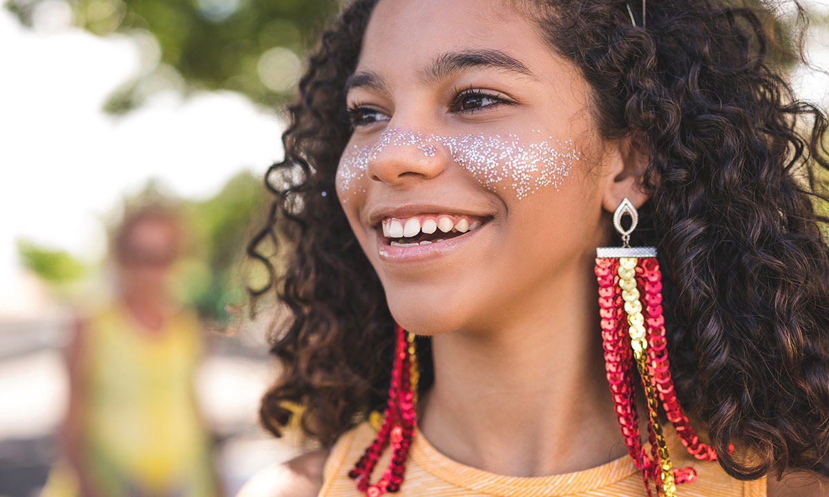 Criança com cabelo encaracolado e glitter e maquiagem no rosto durante Carnaval