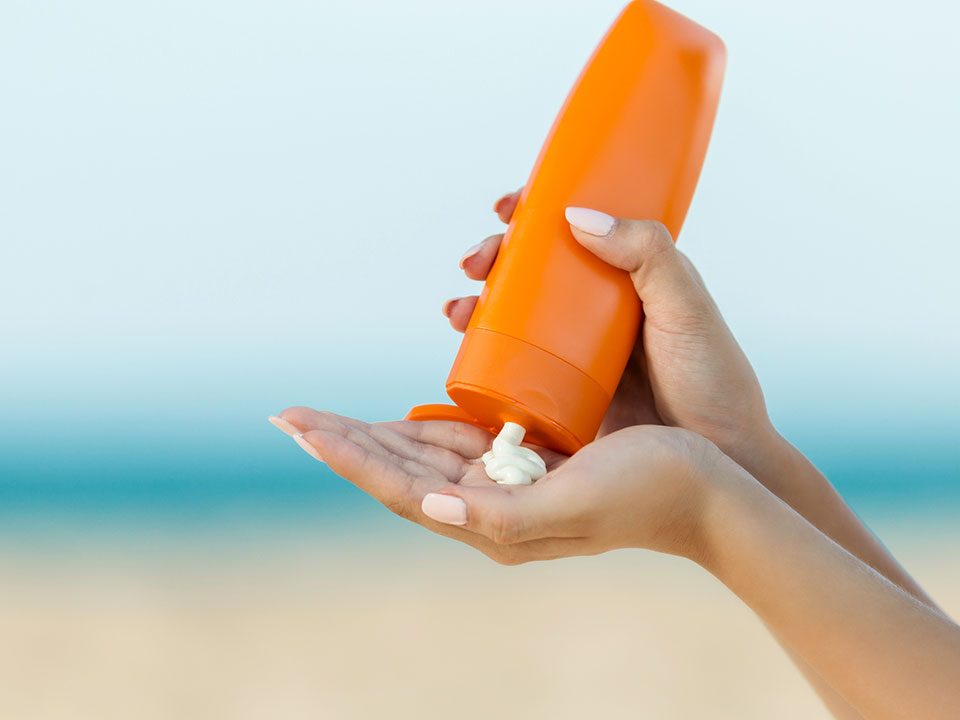 Protetor solar laranja com fundo de uma praia