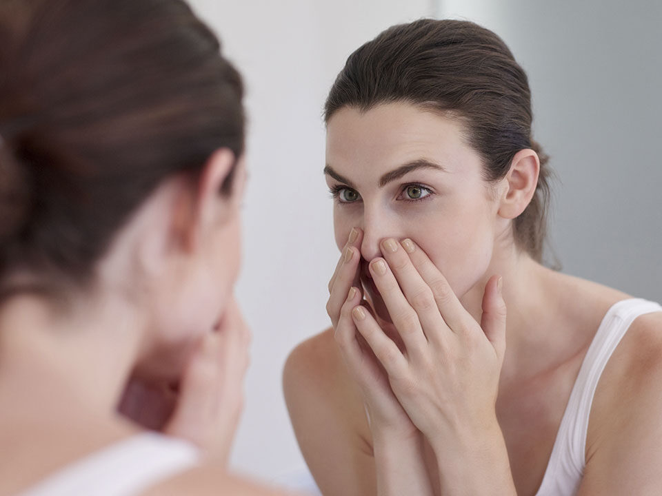 Mulher reparando nos poros dilatados da pele ao se olhar no espelho