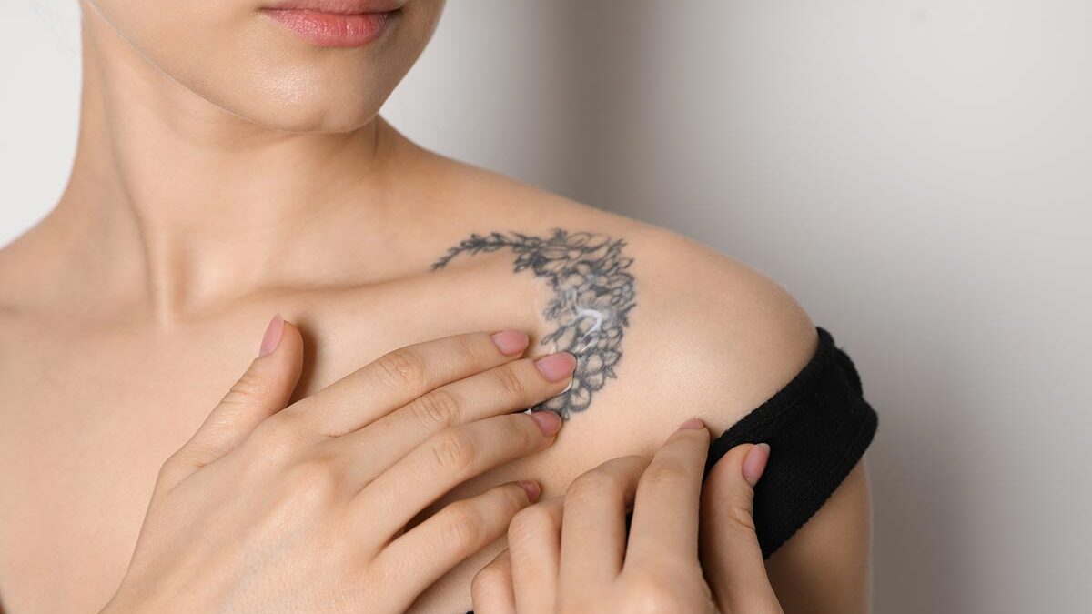 Mulher com a mão sob a tatuagem no ombro