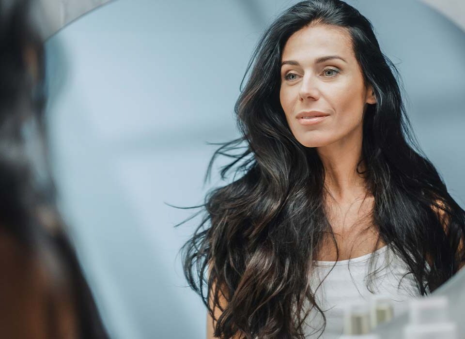 Mulher se olhando ao espelho com olhar preocupado